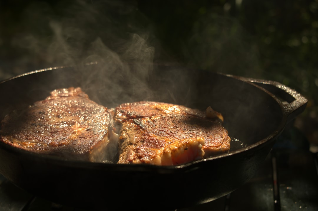 Two steaks searing in a cast iron skillet with steam rising — Flavor Index Lab