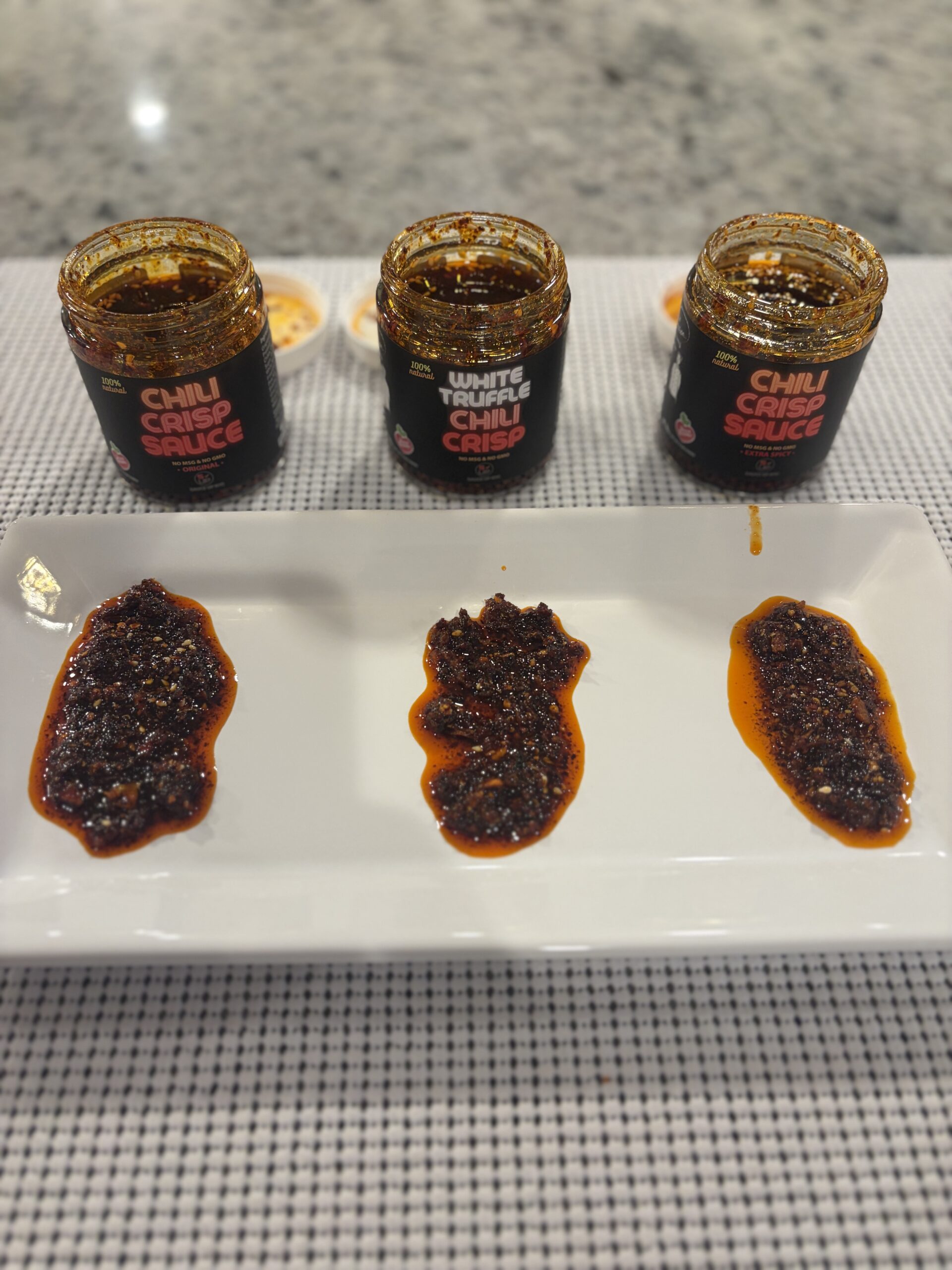 Sauce Up NYC Original, Extra Spicy, and White Truffle chili crisp side by side on plate — Flavor Index Lab