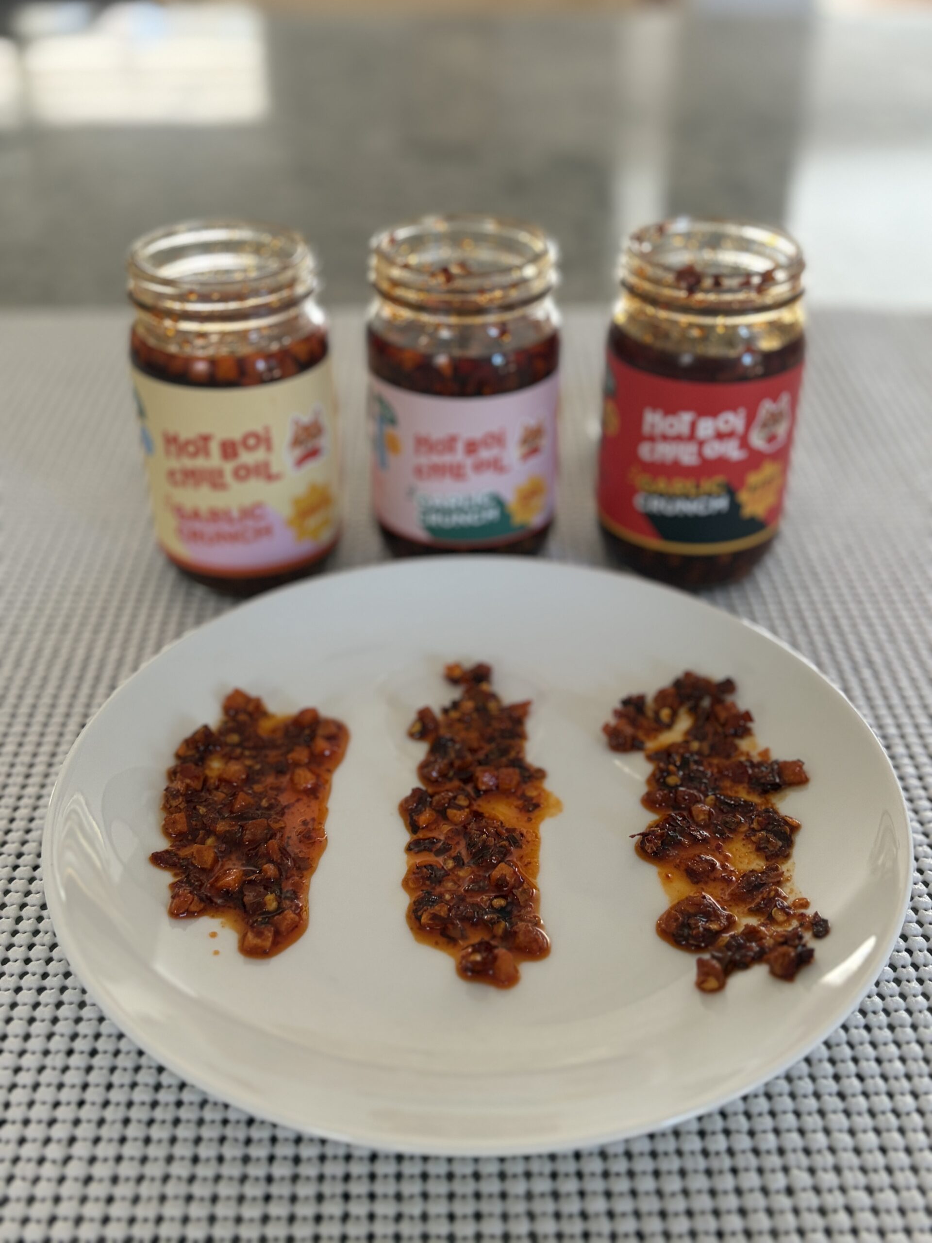 Hot Boi Chili Oil Mild, OG, and Fire jars behind a plate of all three — Flavor Index Lab