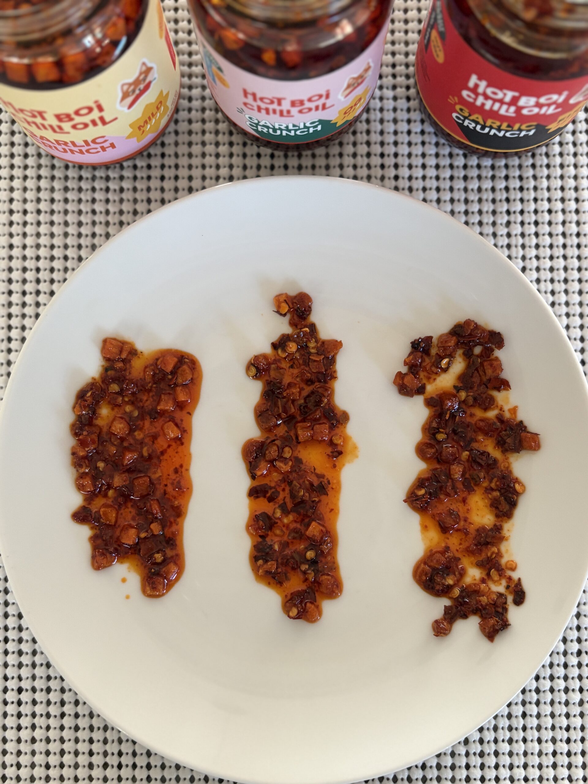 Close-up of Hot Boi Chili Oil Garlic Crunch varieties on a plate showing garlic chunks — Flavor Index Lab